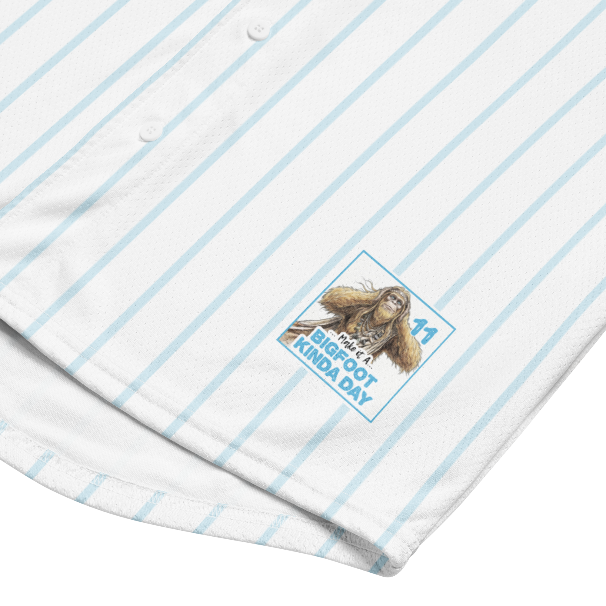 Close-up of a shirt with a cartoon Sasquatch design and text on a white background with blue stripes.